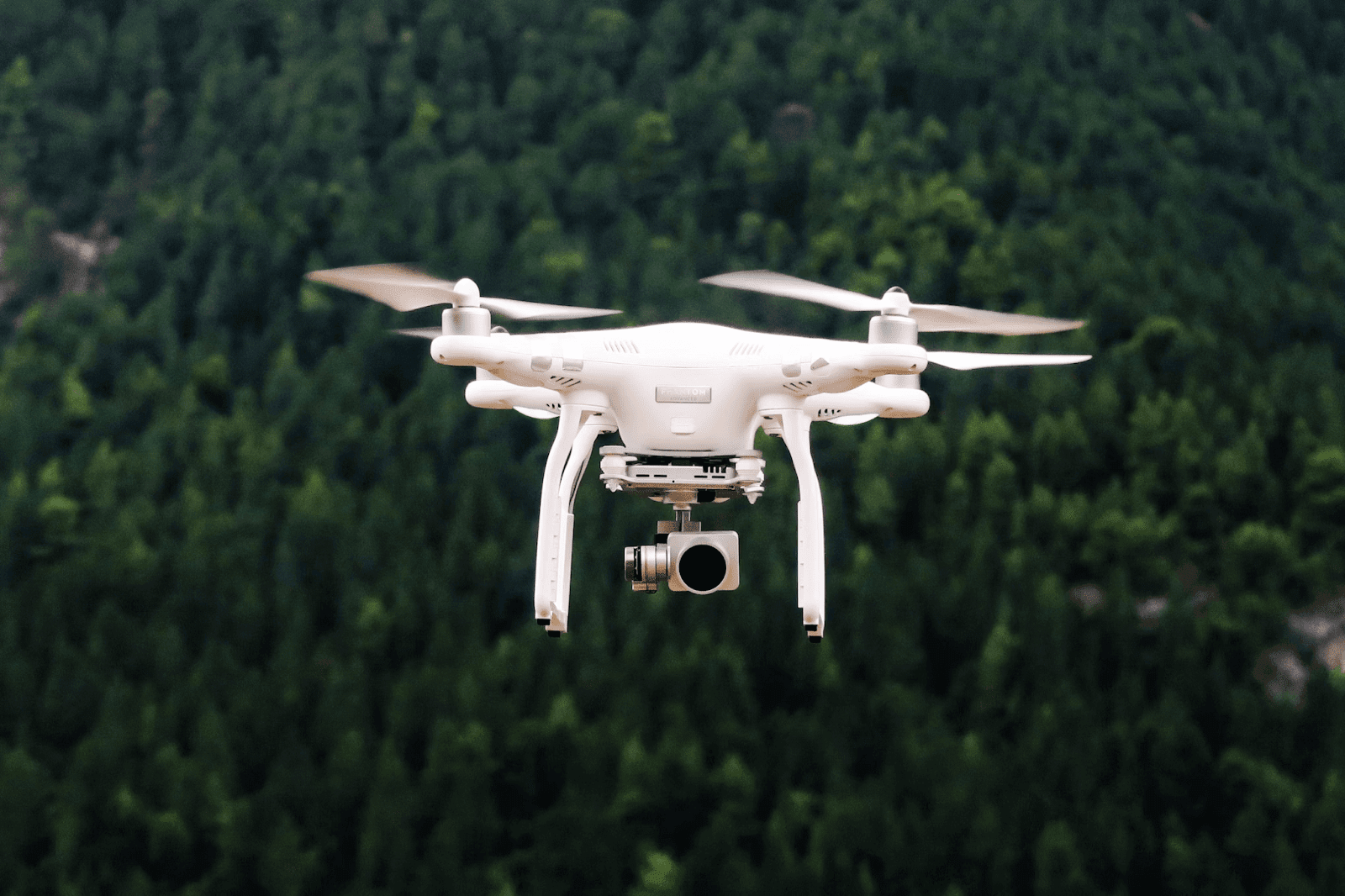 White DJI drone flying over a forest